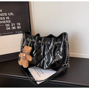 Detail of black quilted tote bag with silver chain strap and a cute bear bag charm