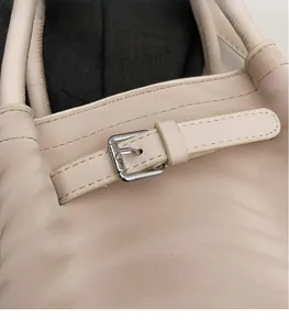 Close-up of beige leather bag with polished silver metal buckle and precision stitching