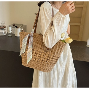 Detail of woven straw tote bag with silk scarf decoration and brown leather handles