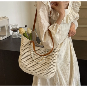 Detail of cream woven tote bag featuring pearl handle and brown leather shoulder straps