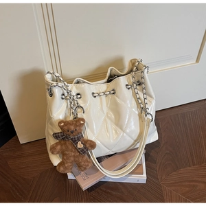 Detail of quilted creamy white tote bag with silver chain strap and plush bear charm