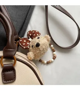 Detailed view of beige plush bear charm with polka dot bow on a cream leather handbag
