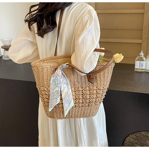 Detail of woven straw handbag featuring leather handles and decorative floral silk scarf