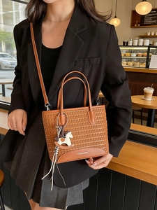 Borsa tote marrone intrecciata con ciondolo a cavallo mostrata in un caffè moderno