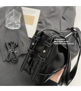 Detail of adjustable straps and silver rivets on a glossy black leather shoulder bag