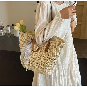 Close-up of woven straw tote bag featuring brown leather straps and a colorful silk scarf