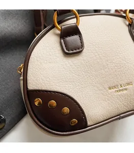 Detail of cream lychee leather Boston bag with brown trim and gold rivet accents