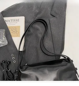Detail view of a black glossy shoulder bag on a grey suit with minimalist aesthetic