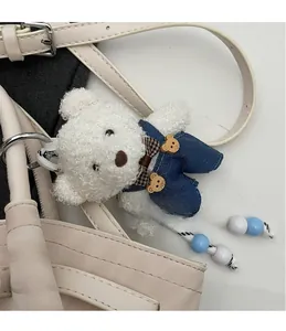 Close-up of white teddy bear charm with blue denim overalls on an off-white handbag