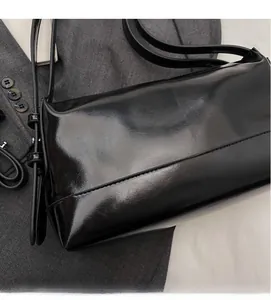 Close-up of black glossy leather shoulder bag on a grey suit jacket for office commute