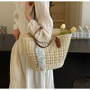 Close-up of woven straw tote bag with brown leather straps and elegant floral silk scarf detail