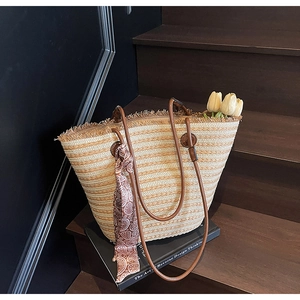 Detail of straw tote bag featuring decorative fringe and a red paisley patterned silk scarf