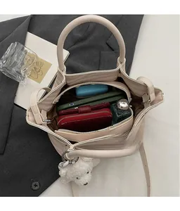 Detail view of cream handbag interior with multiple compartments and plush bear charm