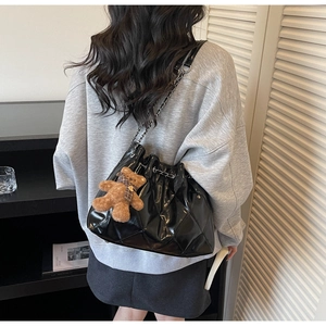 Detail of black quilted bucket bag with chain strap and cute bear charm on a model