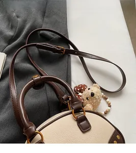 Detail of contrast stitch handbag with bear charm and golden ring hardware on gray blazer