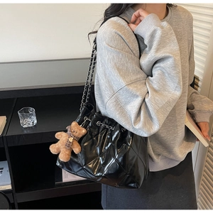 Detail of black quilted drawstring bucket bag with metal chain strap and bear charm