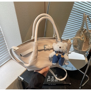 Detail of cream leather handbag with belt strap and cute teddy bear charm accessory