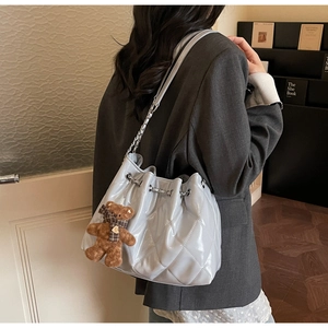 Close-up of quilted bucket bag featuring a silver chain strap and a cute bear charm