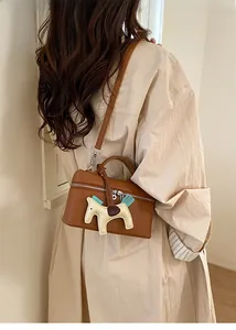 Détail d'un sac à main marron à motif litchi avec un accessoire de charme en cheval