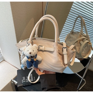 Detail of cream handbag with buckle strap and plush bear charm in a chic interior