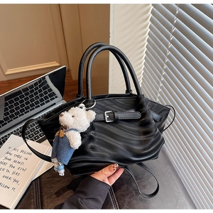 Detail of black wave texture handbag featuring a cute plush bear charm and gold hardware
