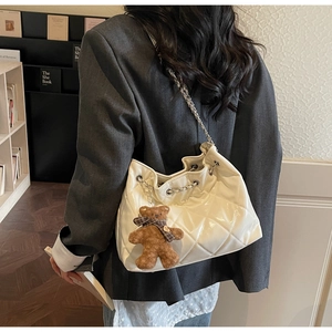 Detail view of a white quilted bucket bag with chain strap and a brown teddy bear charm