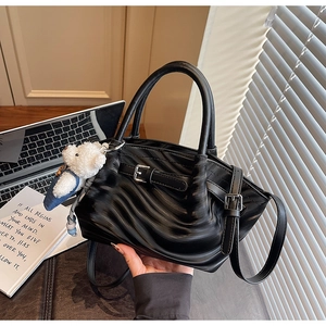 Detail of black wave-textured handbag with white teddy bear charm and round handles