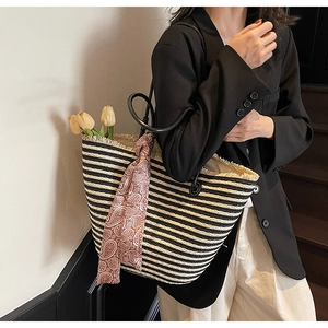 Close-up of a striped straw tote bag featuring tassel edges and a paisley silk scarf detail