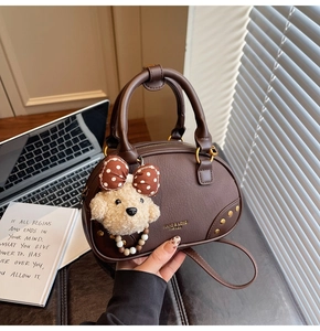 Brown faux leather crossbody bag with gold studs and cute plush dog charm on a desk