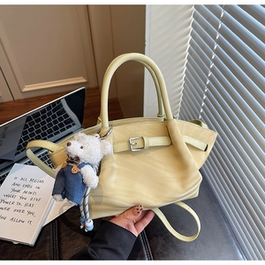 Detail of a creamy yellow handbag with a cute teddy bear charm and adjustable strap