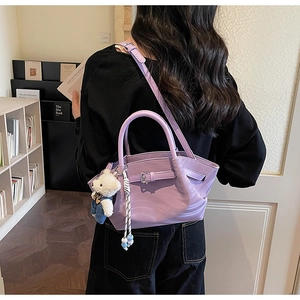 Detail of purple faux leather handbag with belt buckle design and a cute teddy bear charm