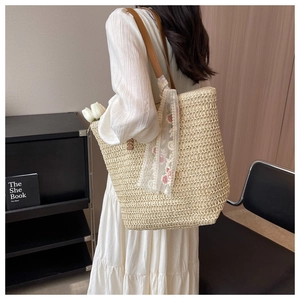 Detail of woven straw bucket bag with floral scarf and leather strap on a model