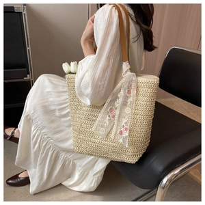Detail of straw woven tote bag with brown straps and floral scarf accent for summer