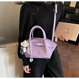 Detail of lavender pleated handbag featuring decorative buckle and cute teddy bear charm