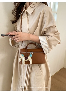 Sac boîte en cuir litchi marron avec bandoulière et breloque cheval porté par un mannequin