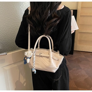 Detail of beige crossbody tote bag with bear charm and braided pendant on model