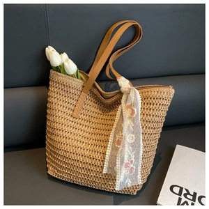 Detail of woven straw tote bag with brown leather handles and a floral lace scarf decoration