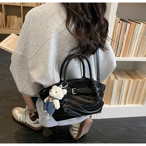 Close-up of black pleated glossy handbag with metal buckle and cute bear charm