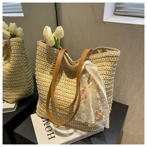 Detail of woven straw tote bag featuring brown leather straps and floral lace scarf accent