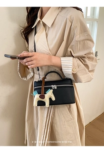 Détail d'un sac à main noir en cuir grainé avec forme boîte vintage et breloque cheval