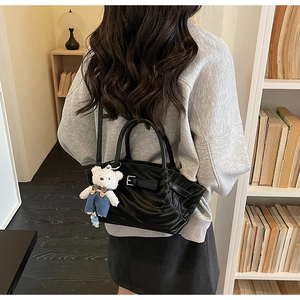 Detail of black pleated handbag with a cute white bear charm in a cozy library setting