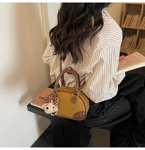 Close-up of a yellow Boston handbag with leather handles and a cute brown plush bear charm