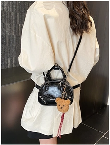 Detail of black glossy shell bag with silver rivets and a cute brown teddy bear pendant
