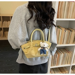 Detail of light yellow leather handbag with cute bear charm and adjustable shoulder strap