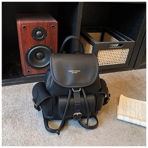 Detail of black pebbled leather backpack showing flap closure and external utility pockets