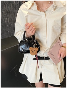 Detail of black glossy shell bag with silver rivets and a cute brown plush bear charm