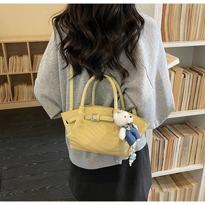 Detail of yellow leather handbag with cute teddy bear charm on a library bookshelf backdrop