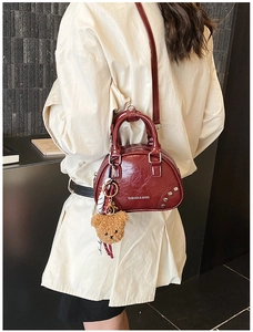 Detail of wine red glossy patent leather bag with rivet accents and teddy bear charm