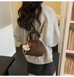 Close-up of brown PU leather pillow bag featuring metal rivets and a cute dog charm