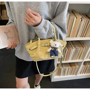 Close-up of yellow handbag featuring a leather strap buckle and cute teddy bear charm